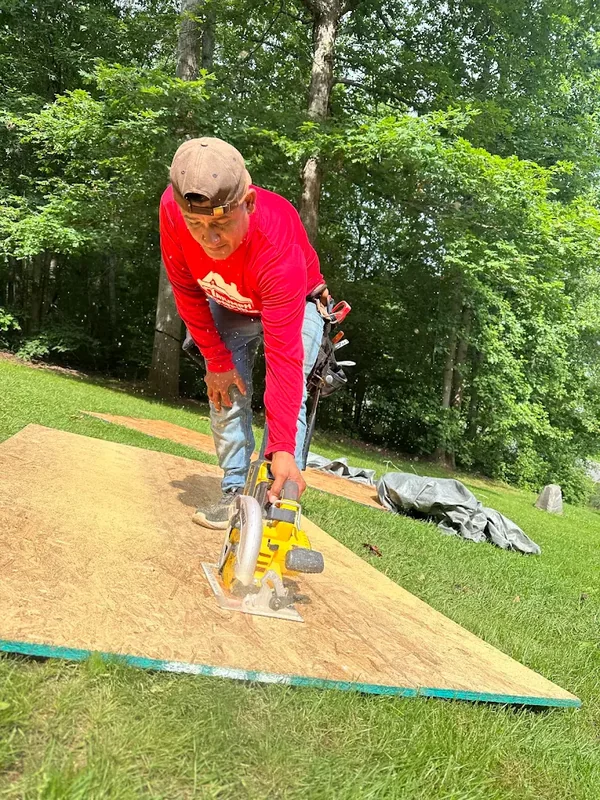 Crew member in a red Triumph Roofing shirt cutting roof decking